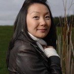 Dr. Chau Pham stands under a grey sky. she's in a leather jacket and her right hadn is tugging at the neck of her sweater.