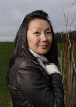 Dr. Chau Pham stands under a grey sky. she's in a leather jacket and her right hadn is tugging at the neck of her sweater. 