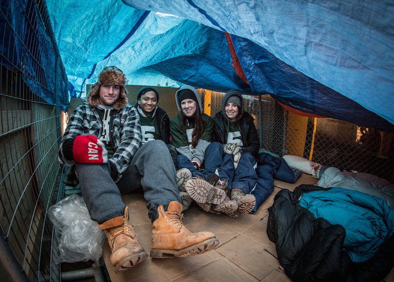 four students sit under a tarp