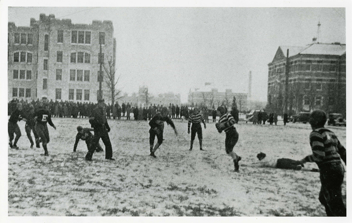 Students playing football on campus in 1936 while a crowd watches in the background.