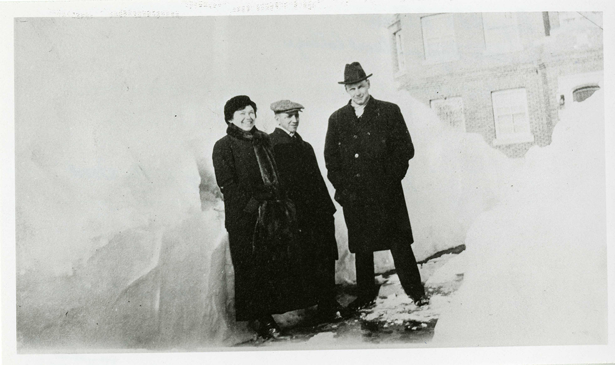 Three people standing beside a large snowdrift in front of the President's House (now known as Chancellor's Hall). Taken sometime between 1915 and 1920.
