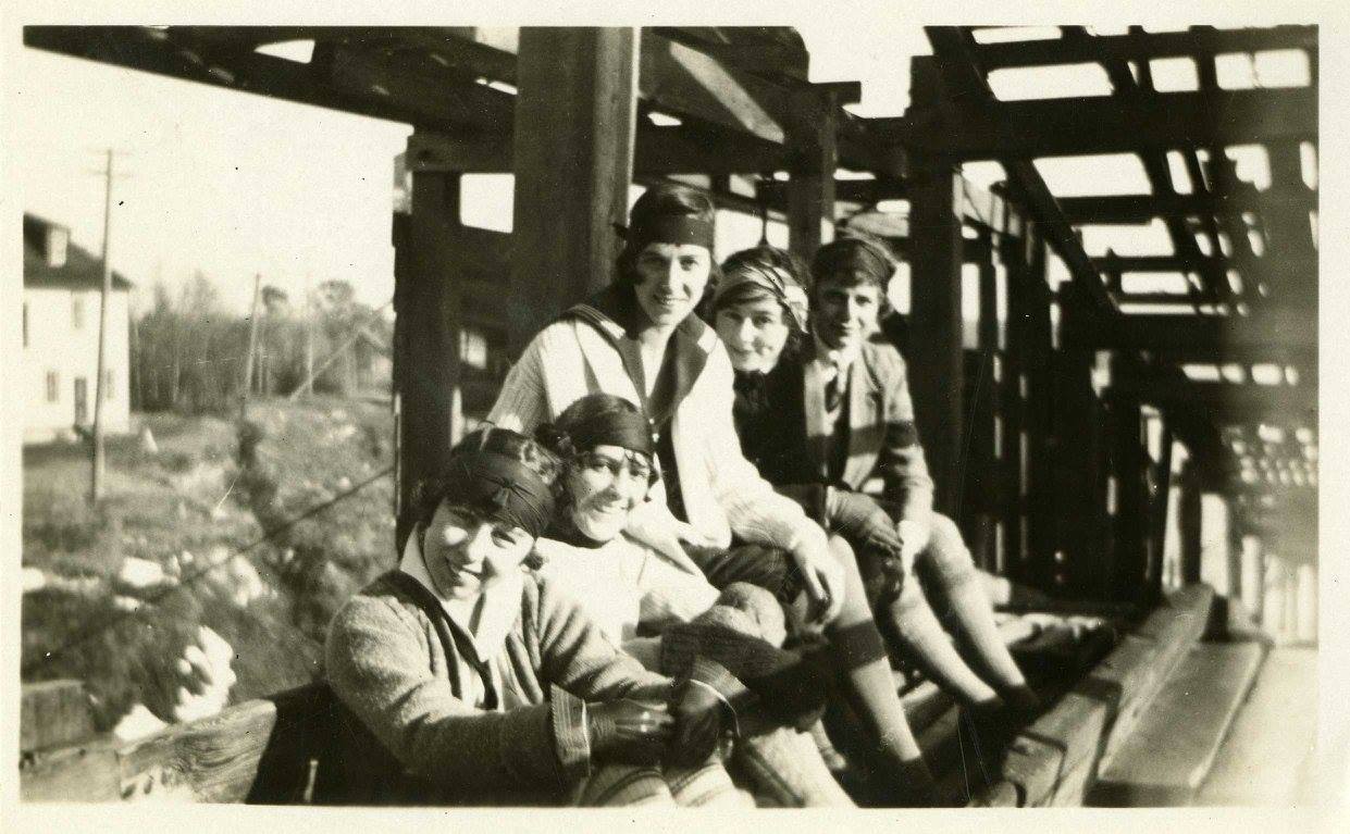 A photograph of five unidentified Manitoba Agricultural College students. The students appear to be sitting below wooden scaffolding on the Manitoba Agricultural College Campus. Photograph is dated as having been taken between 1924 and 1926. Source: University Relations and Information Office fonds.