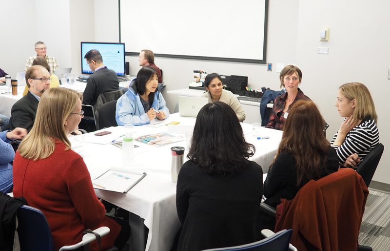 A group sits around the table listening to Jocelyn Thorpe (at far head of table on the right) as she leads a seminar at the 2017 Teaching Café.