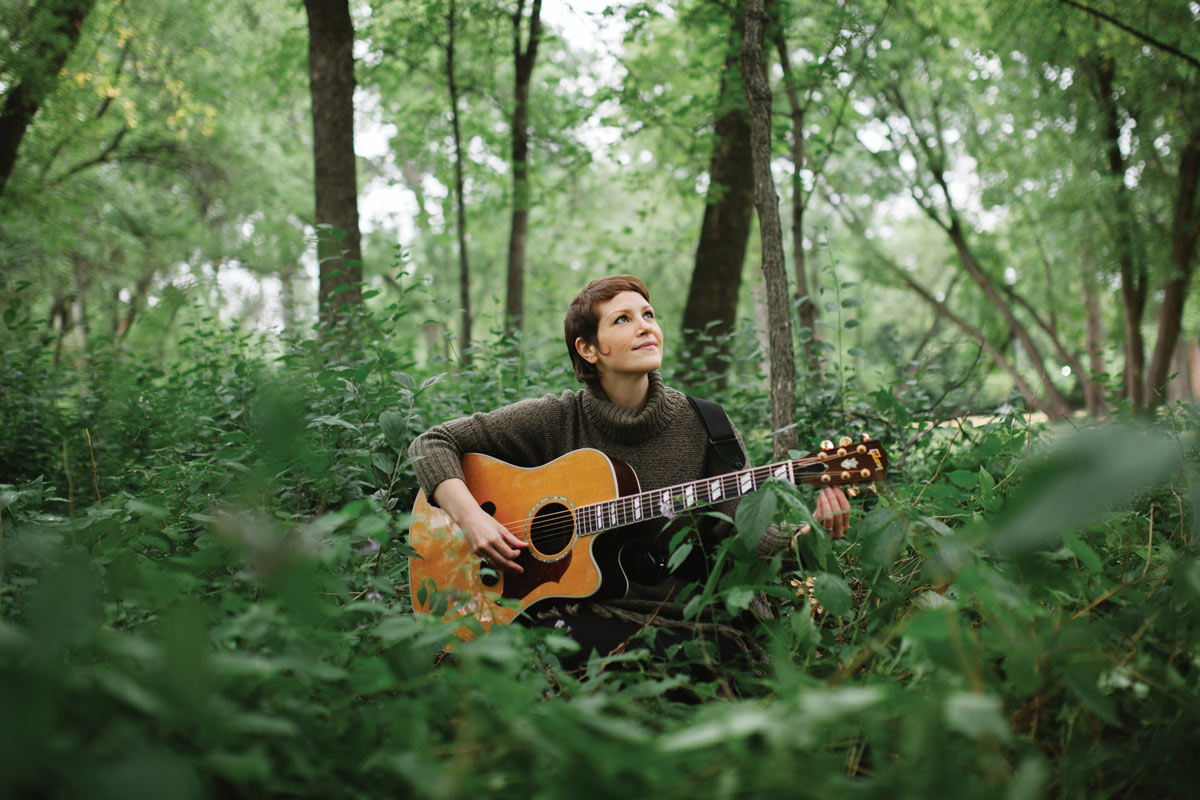 Sheena Grobb plays a guitar in a dense, green forest