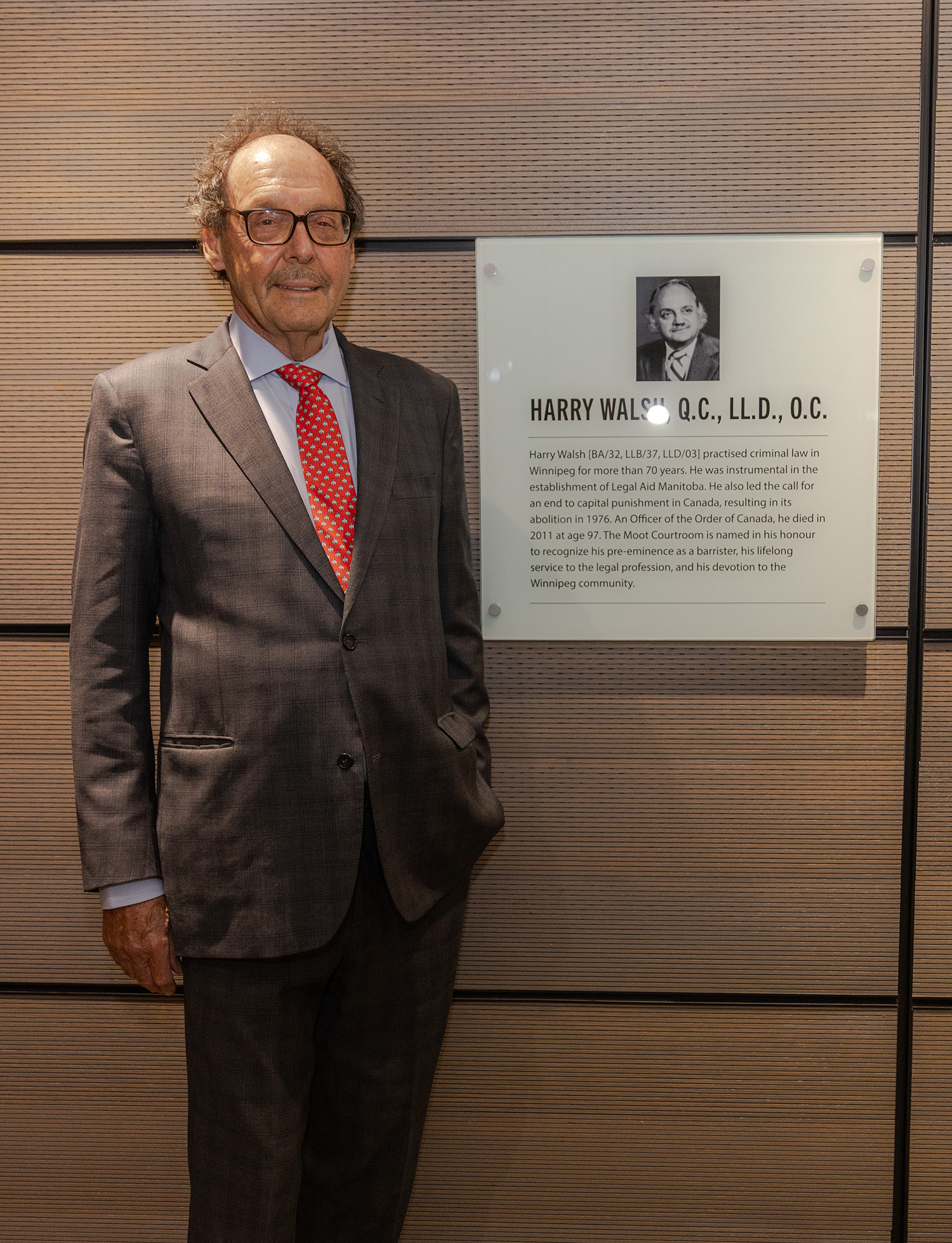 Ron Stern, nephew of Harry Walsh, stands beside the plaque dedicating the Faculty of Law’s Moot Courtroom to his uncle. Photo by Adam Dolman.