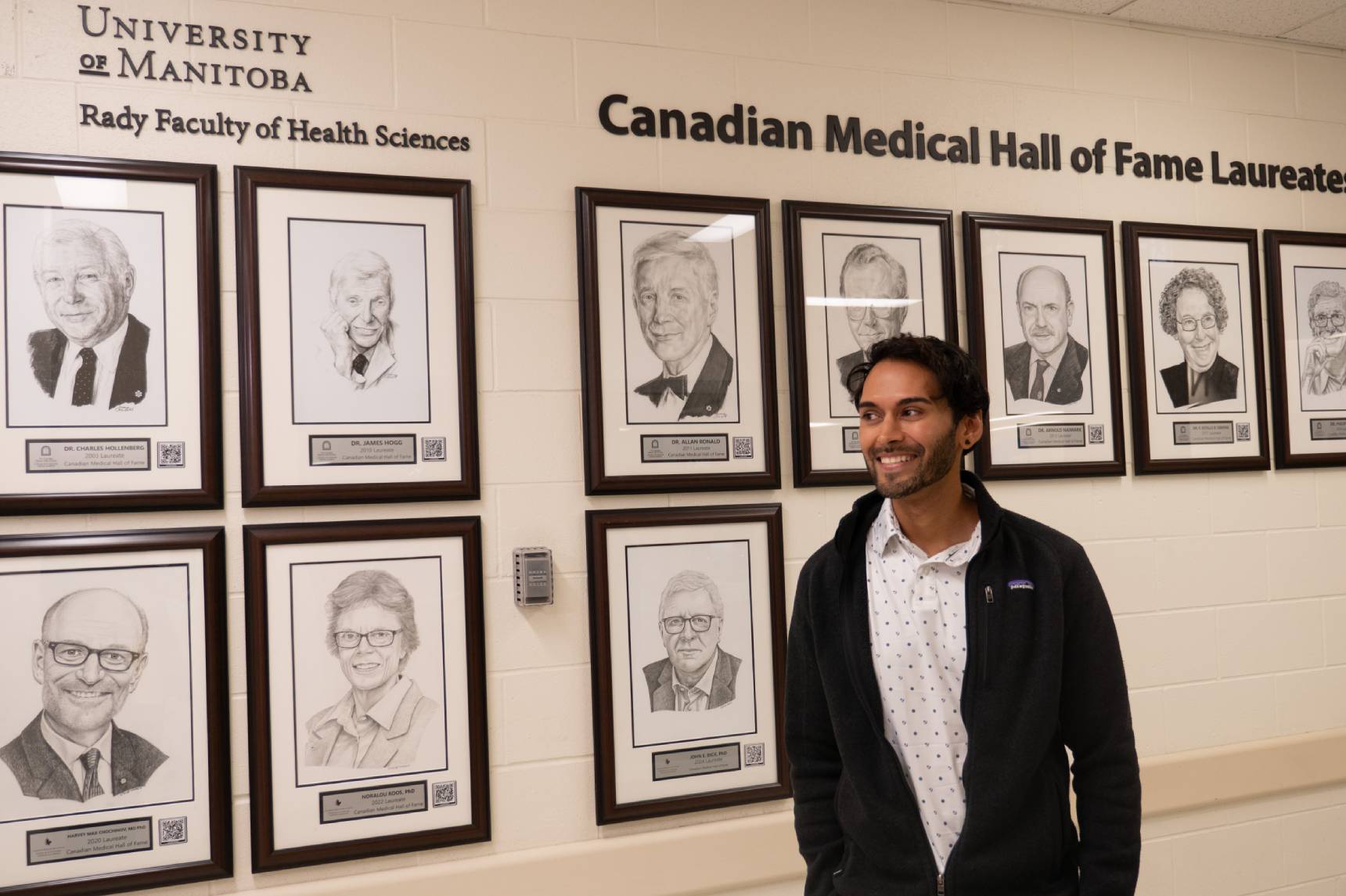 Akhil Ramdoyal smiling and looking to the left, behind him is the UM Canadian Medical Hall of Fame Laureates wall.