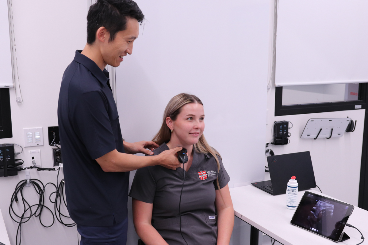Dr. Terry Li uses a POCUS device on another person's neck.