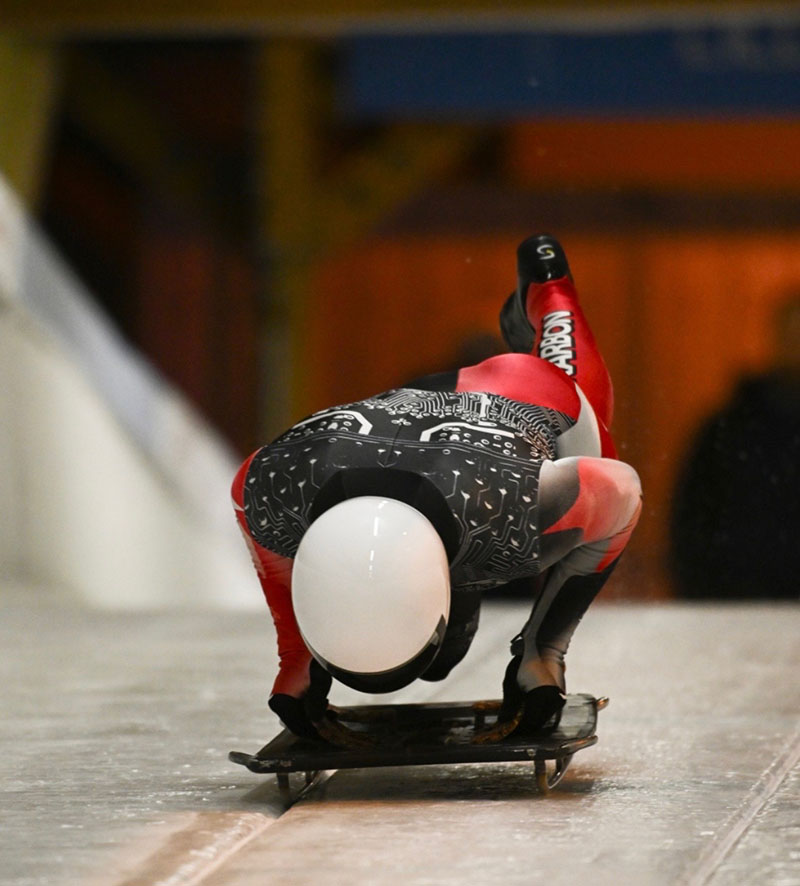 A skeleton athlete jumps onto their sled at the top of a sliding track.