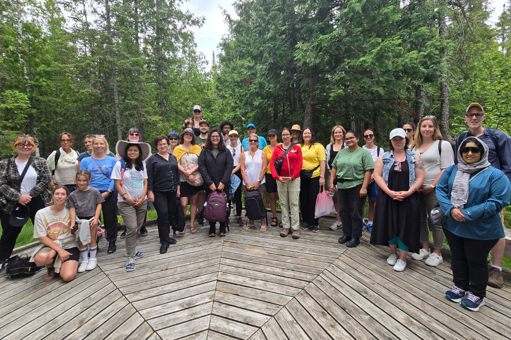 A group of Summer Institute participants posing for a photo on a wooden platform in the forest.
