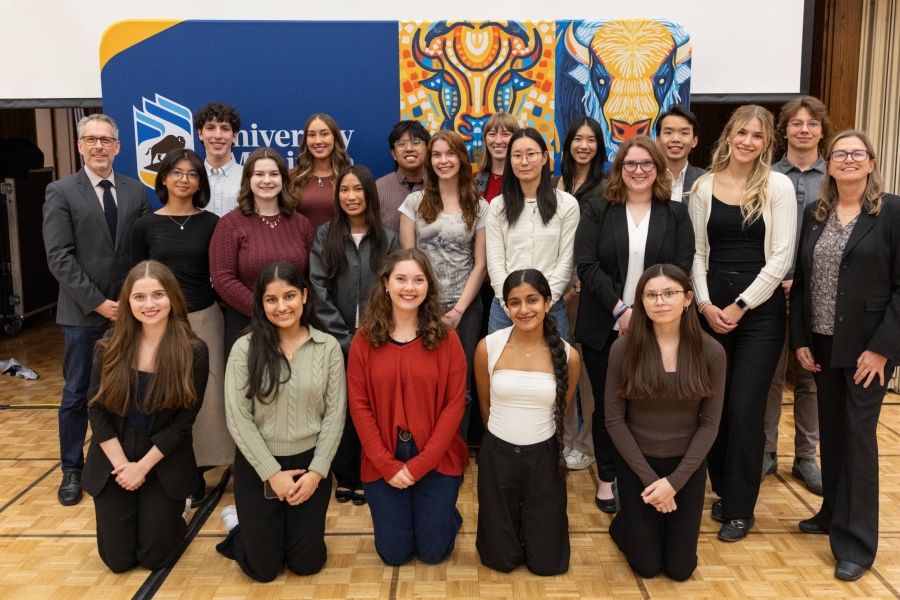 Students pose together with faculty in front of a colourful bison-themed backdrop..