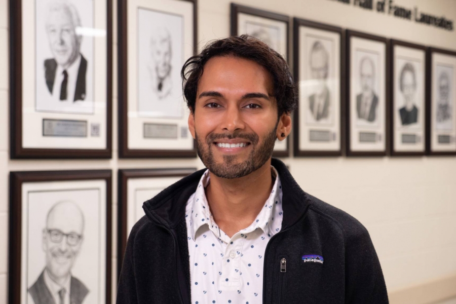 Akhil Ramdoyal smiling in front of the Canadian Medical Hall of Fame Laureates wall at the UM Bannatyne campus.