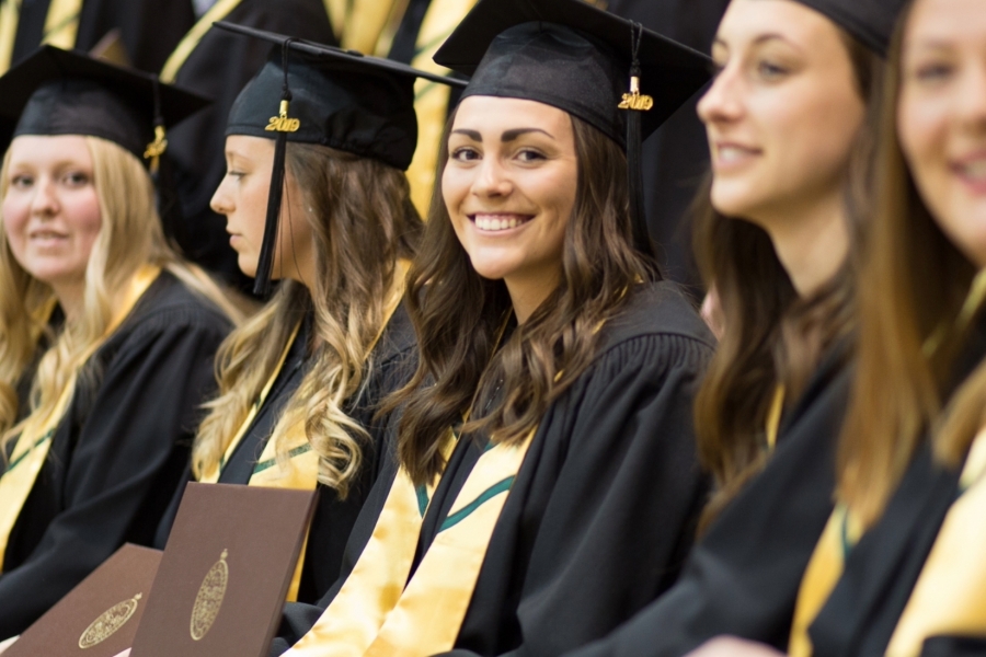 Row of smiling young women in UM cap and gown.
