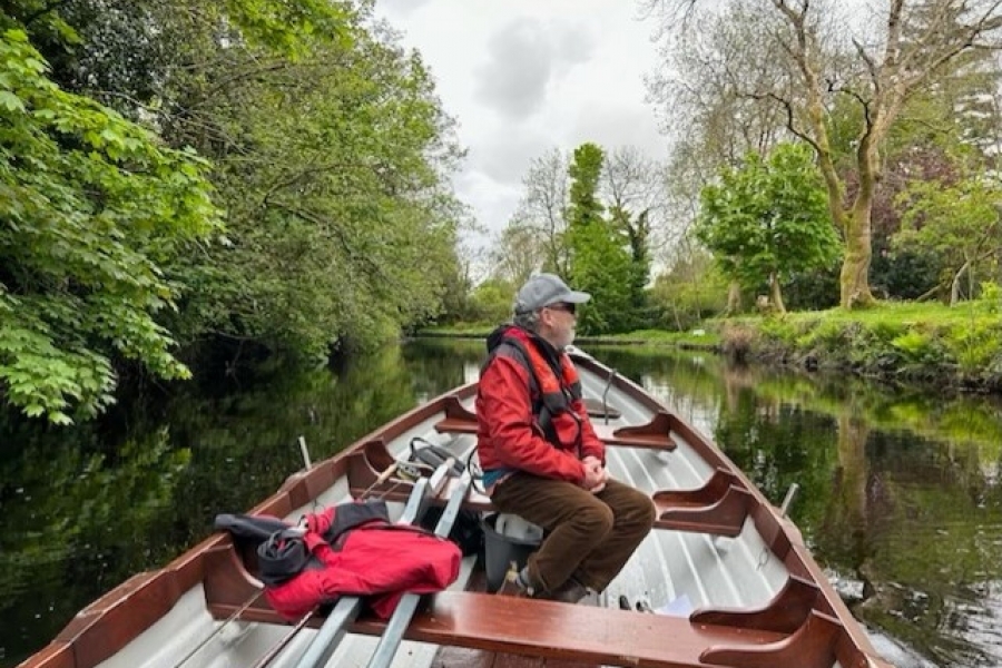 Dr. John Sinclair appears on a boat on top of a river, looking out to the nature surrounding him.