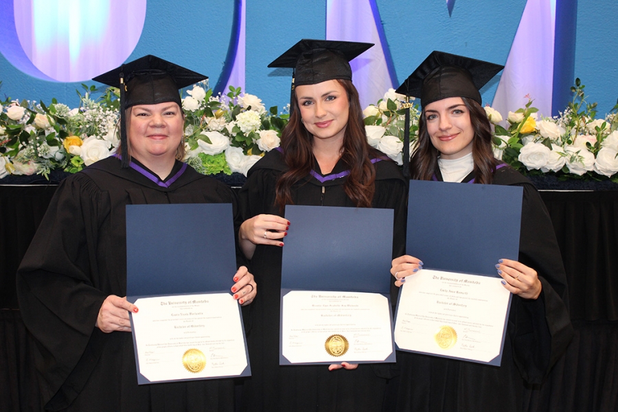 Laura Warkentin, Brooke-Lyn Wahoski and Emily Howarth wearing graduation caps and gowns, holding their degree parchments.