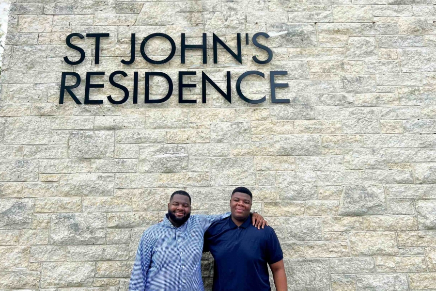 Two people smiling in front of St John's Residence sign.