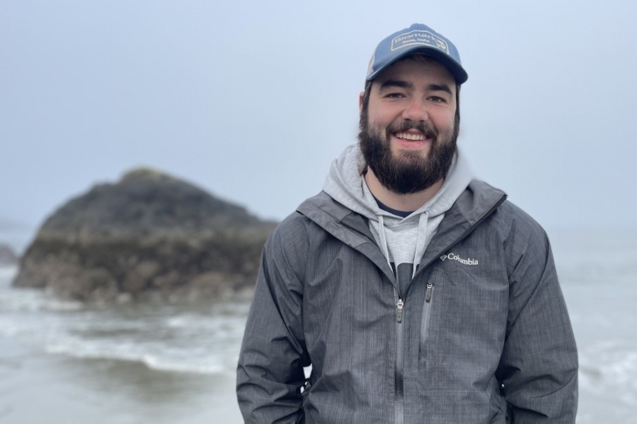 Smiling student poses for the camera infront of a ocean scene.