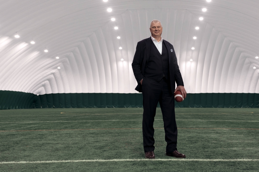 Randy Ambrosie, Commissioner of the CFL, stands on green turf holding a football