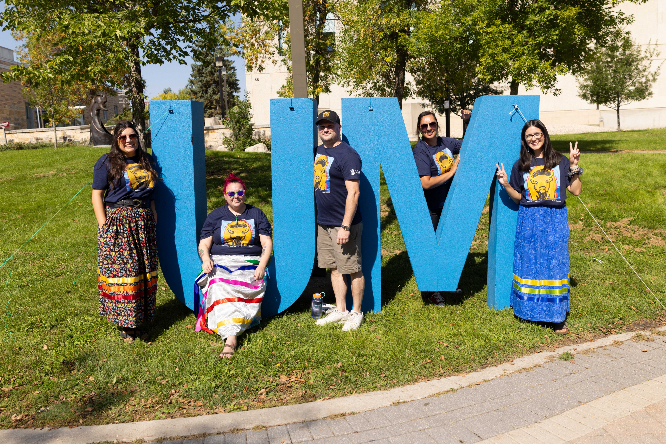 Five people wearing t-shirts with a Peatr Thomas designed bison stand in front of large UM letters.
