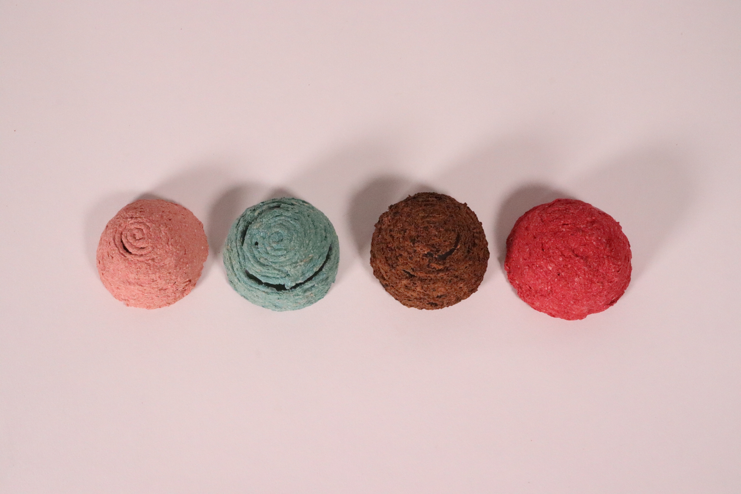 Four round, textured wafers are lined up on a light pink background.