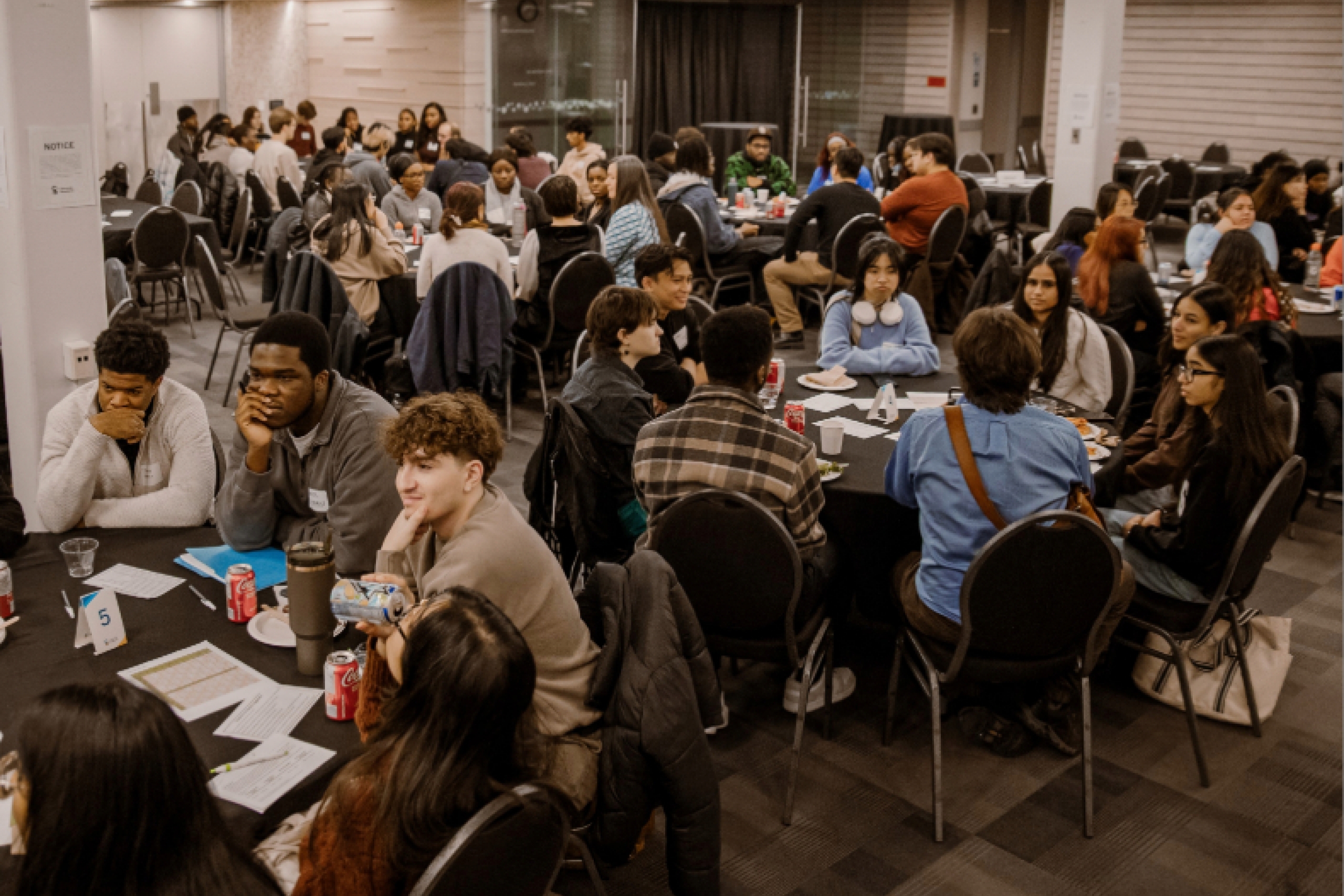 A room of students sitting at round tables, 8 students each.