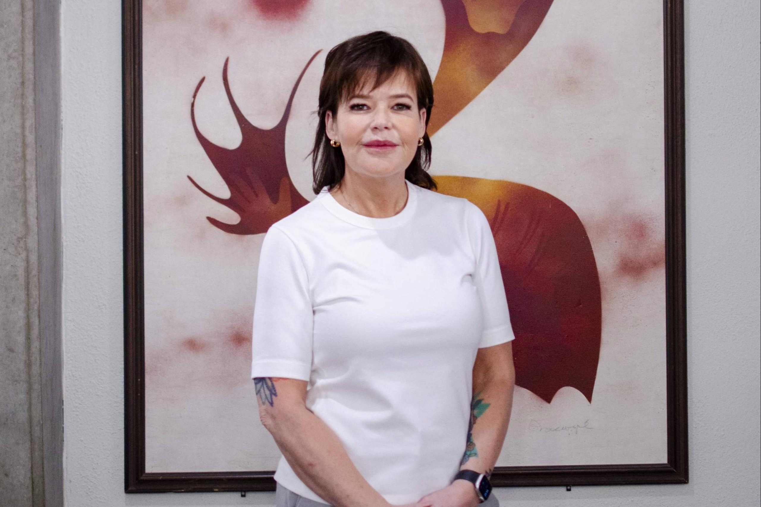 Smiling woman with dark hair stands in front of Indigenous print.