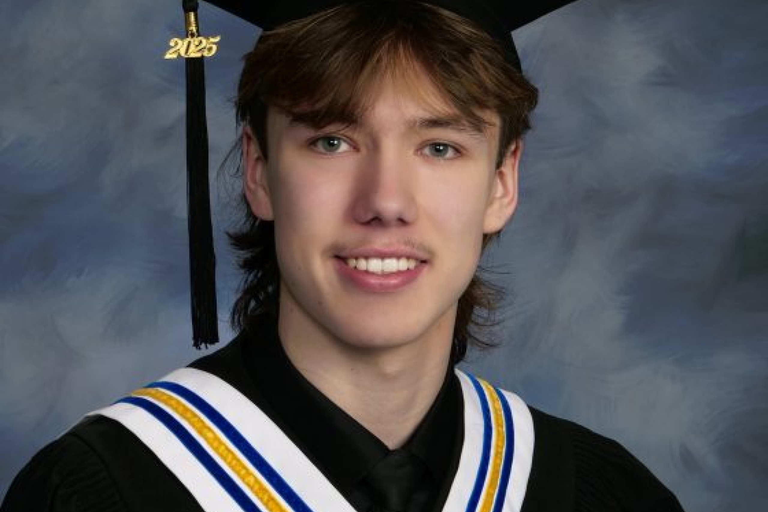 Smiling young man with brown hair in a graduation cap and gown