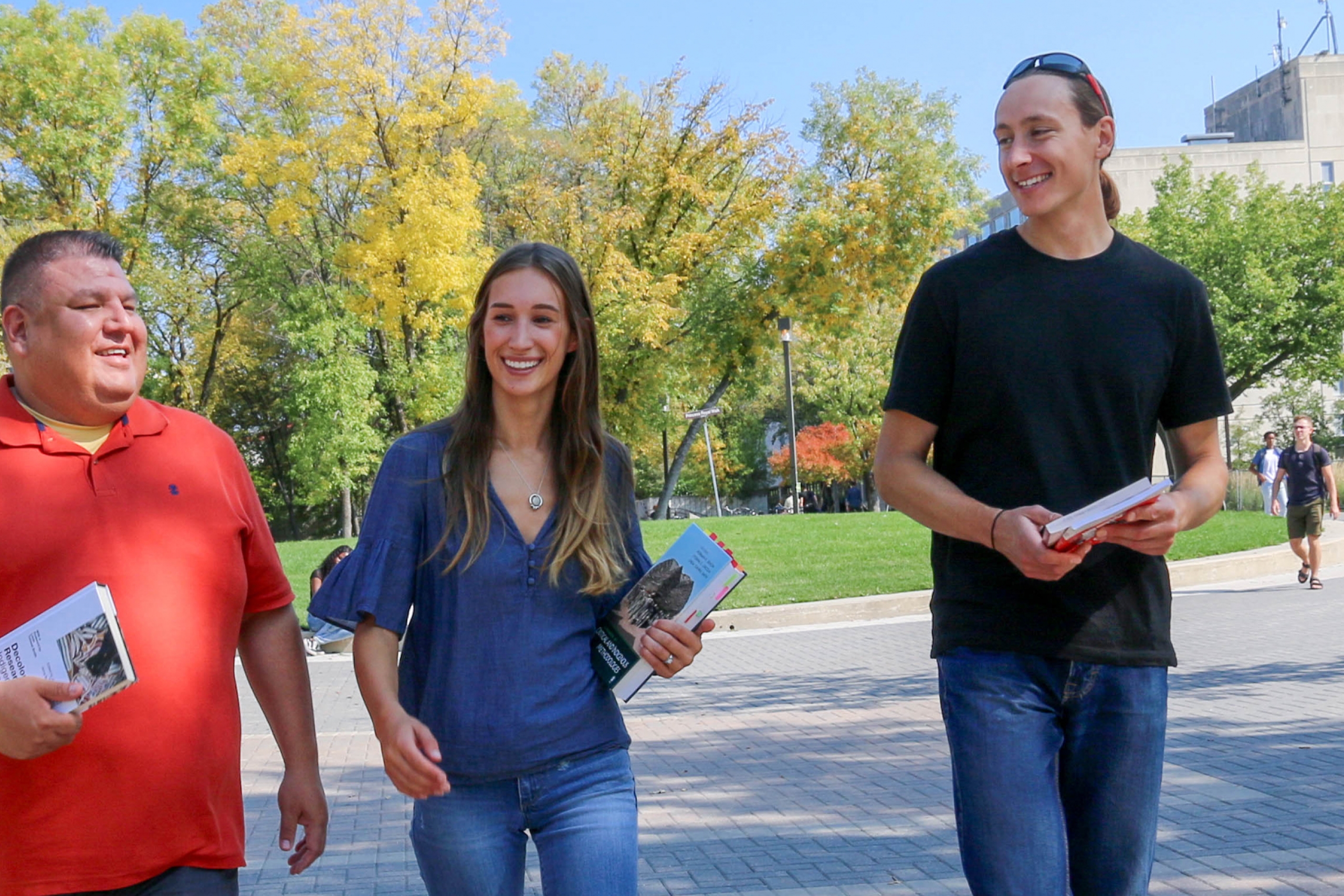 Two men and a woman walk across the UM campus.
