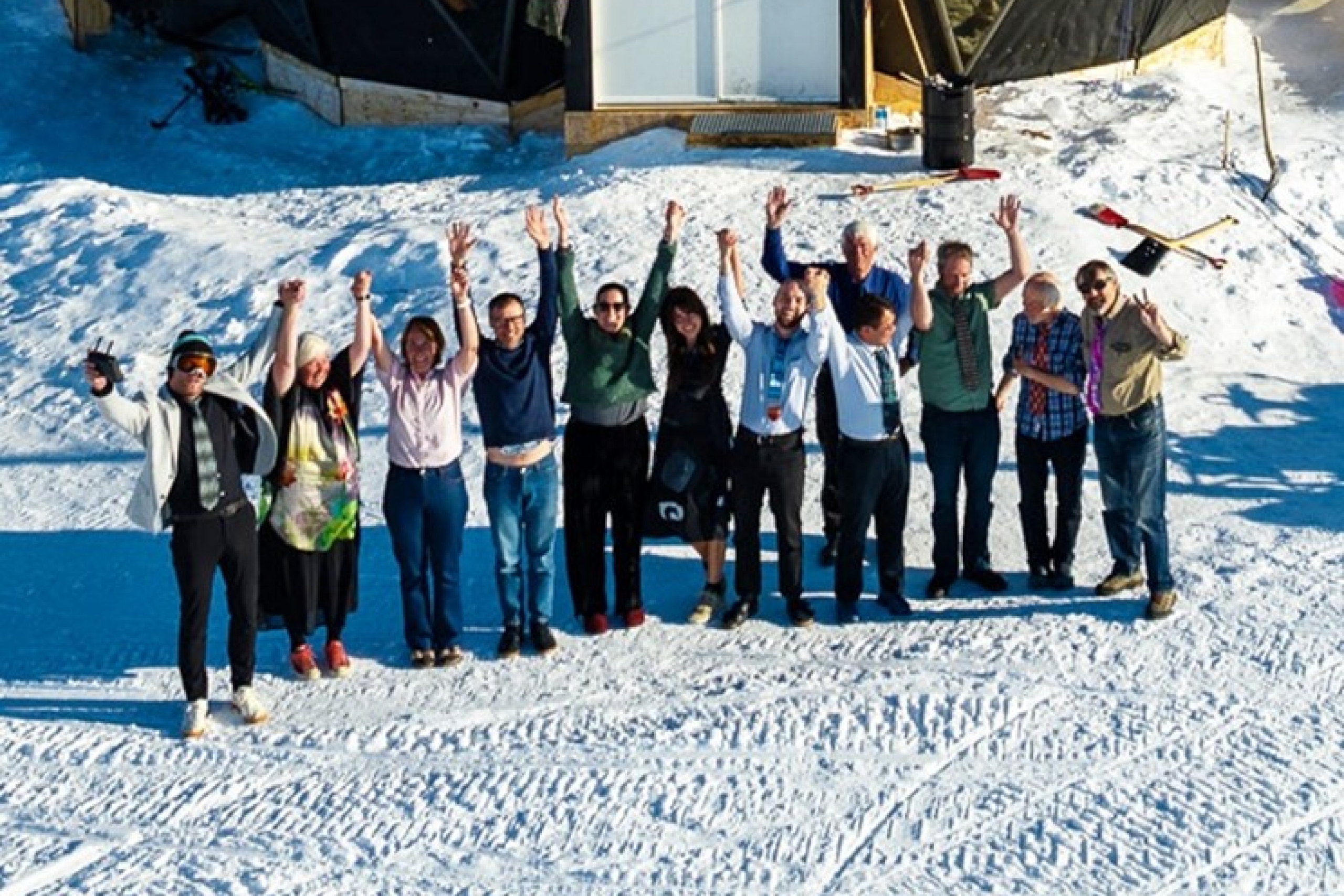 A group of scientists on packed-snow holding their arms up in celebration