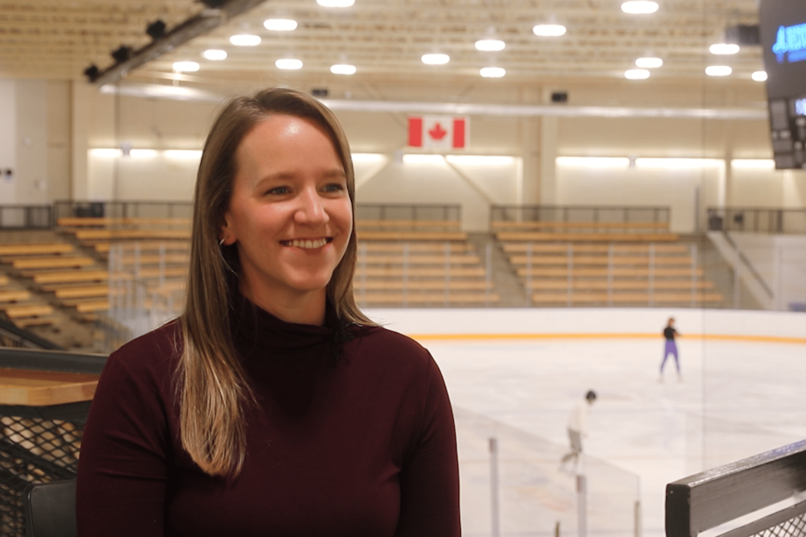 A woman sits in an ice rink smiling at the camera