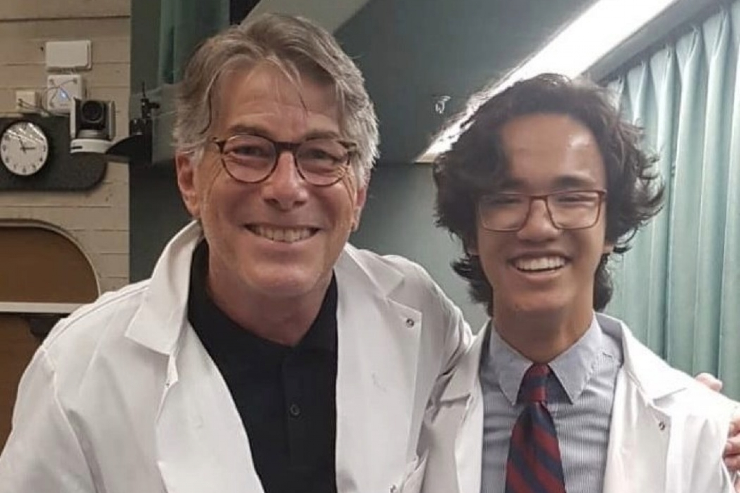 Two individuals in lab coats smiling at the camera.