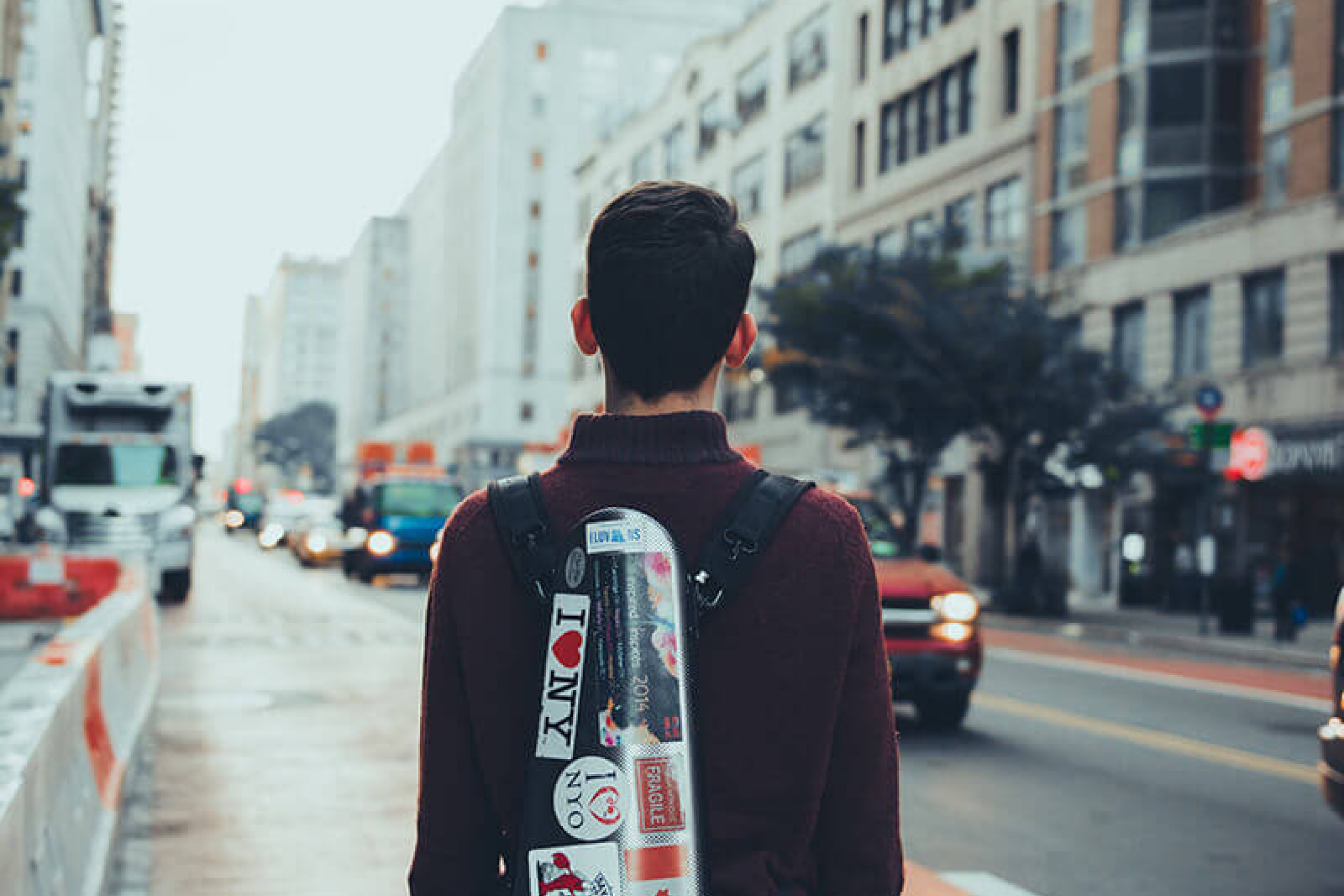 A young man standing on a street holding a violin case covered in stickers.