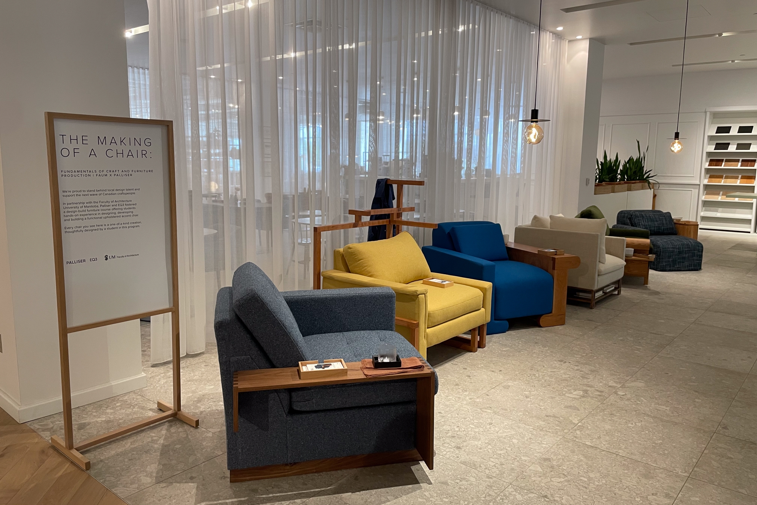 Modern showroom displaying colorful armchairs in blue, yellow, and gray against sheer white curtains. A sign reads "The Making of a Chair," creating a stylish, inviting ambiance.