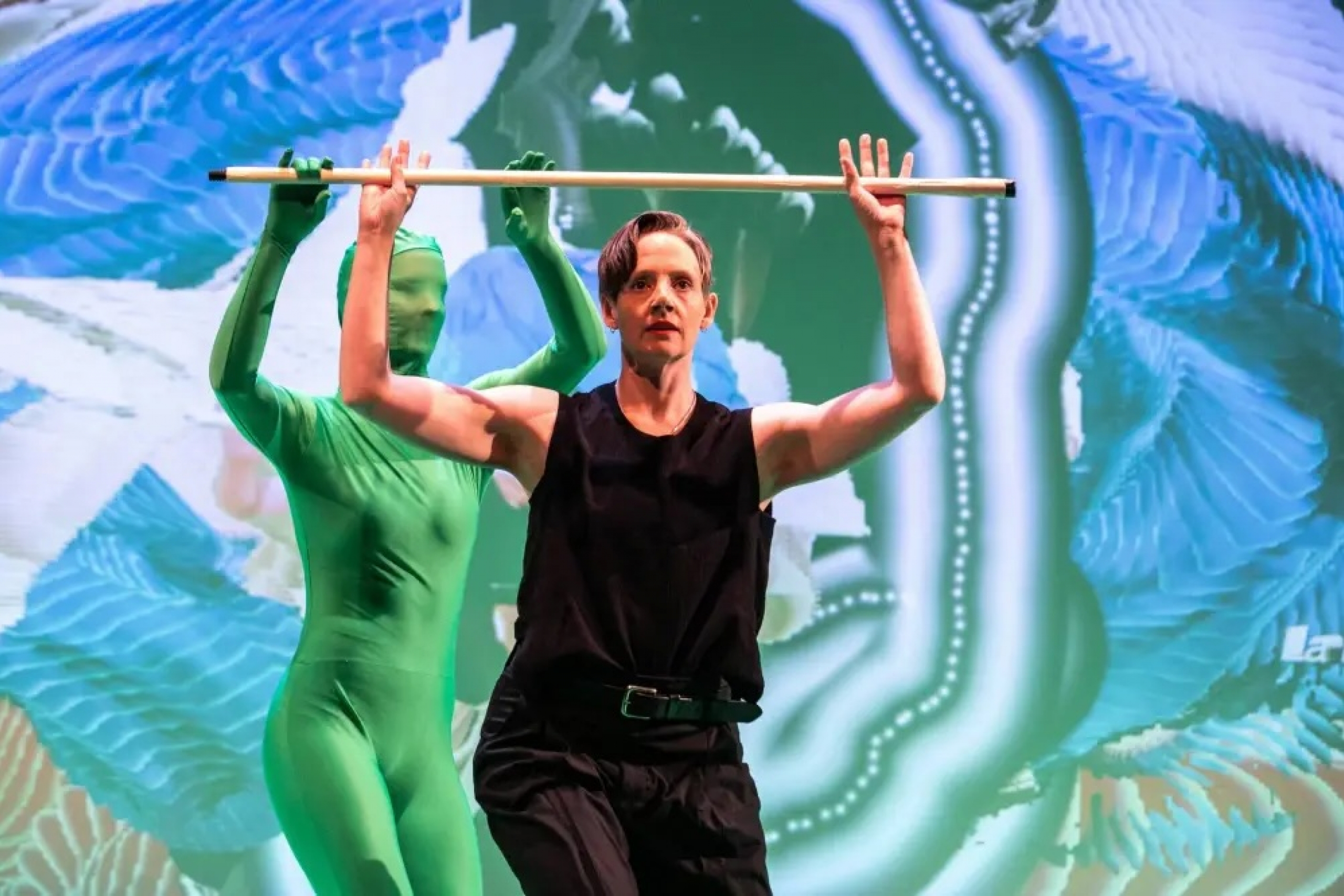 Freya Olafson and Emma Beech mirror a pose with a horizontal pole against projected imagery.