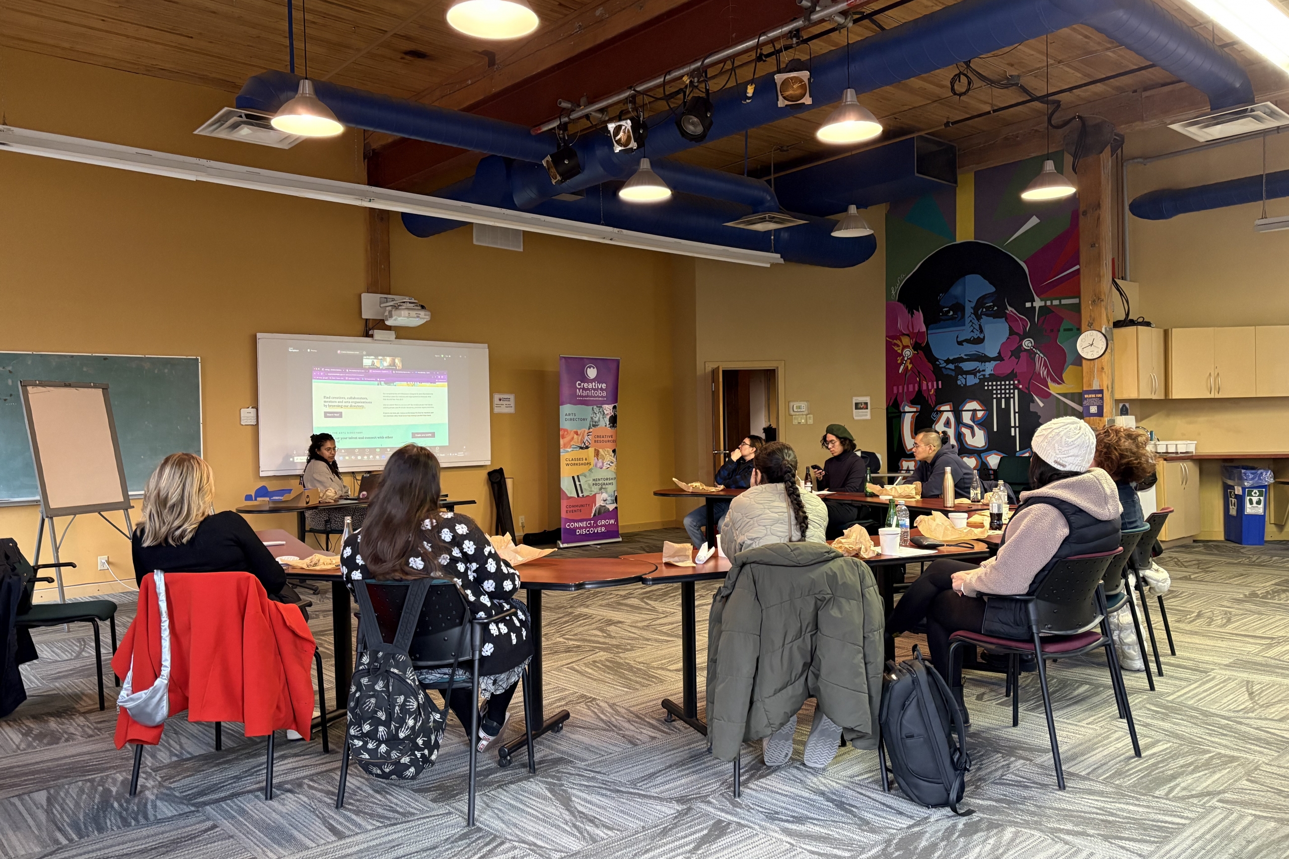 Students at Ignite sitting at tables listening to a speaker who is presenting at the front of the room.