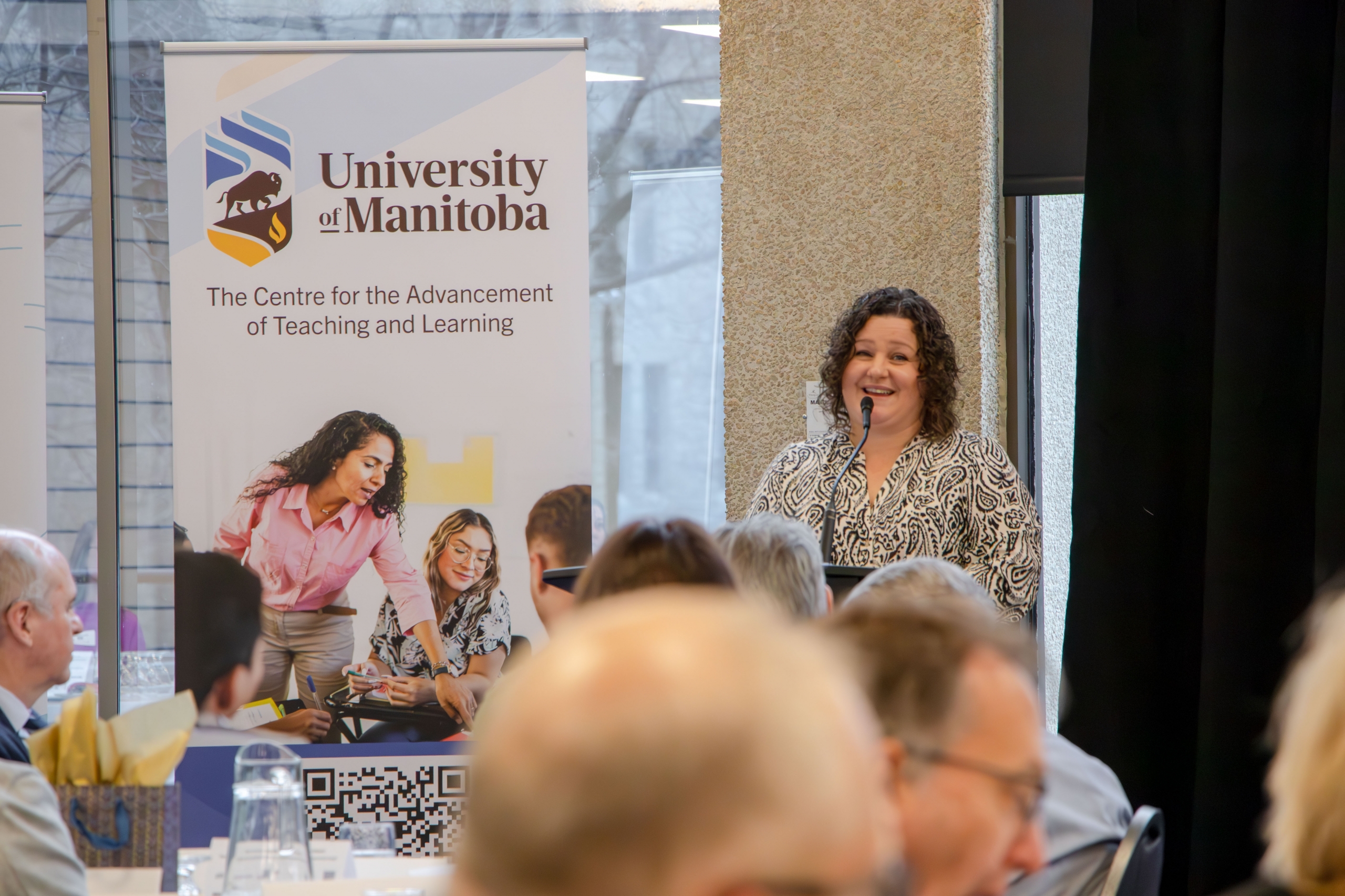 Janine Carmichael speaking on stage behind a podium at the Faculty Symposium.
