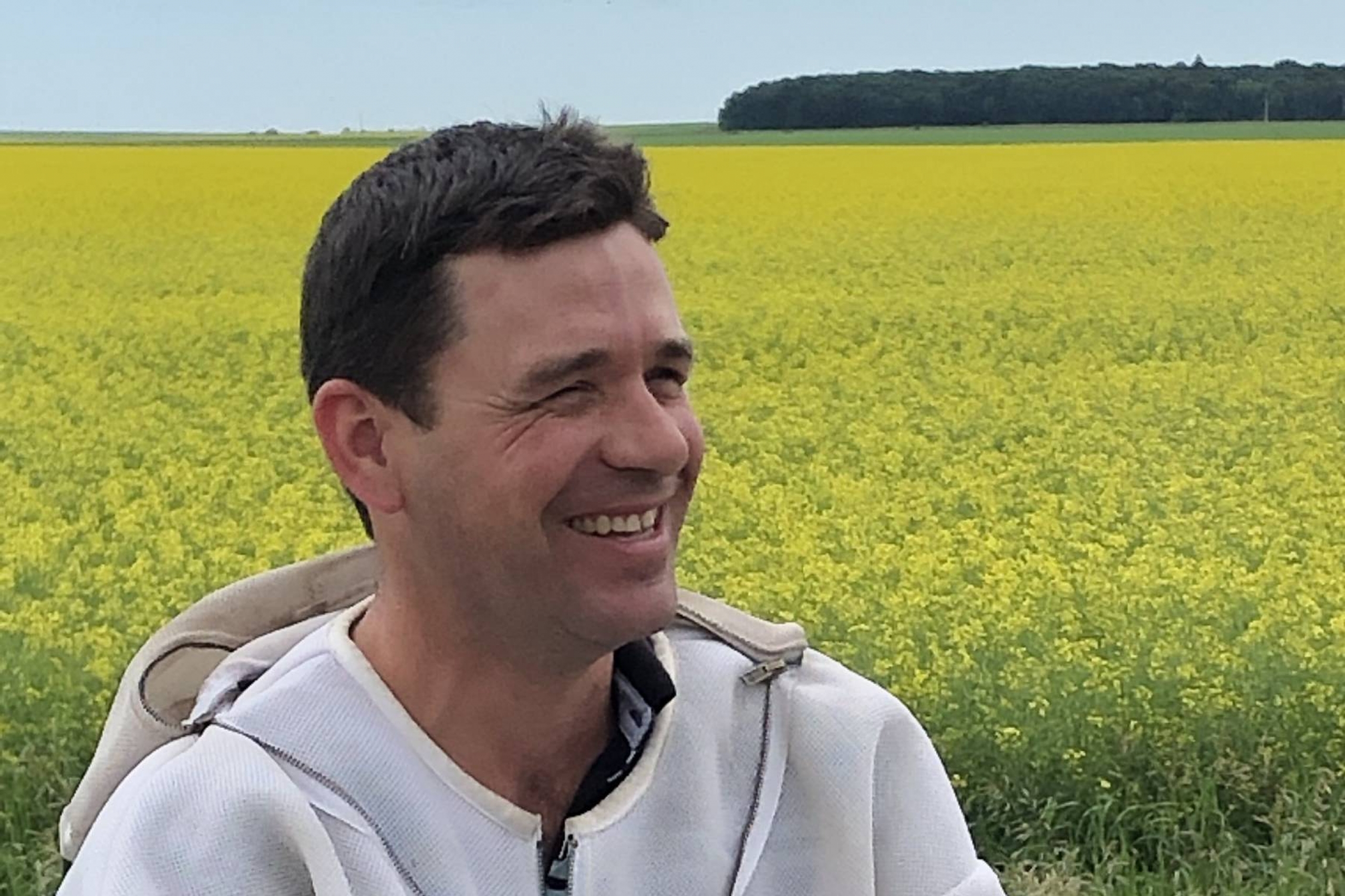 Ian Steppler wearing a bee suit in front of a field of canola.