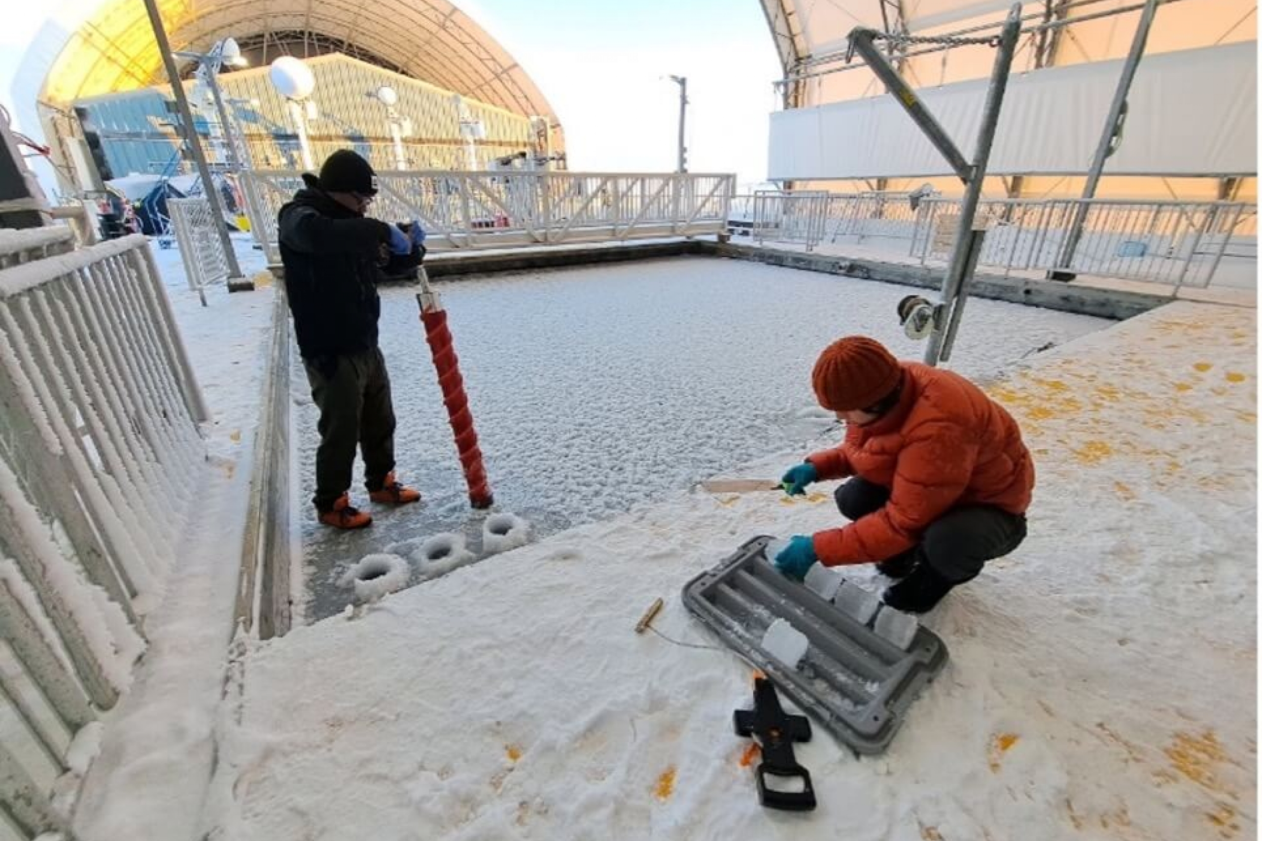 Two researchers are using a drill to pull out ice core samples from the testing site.