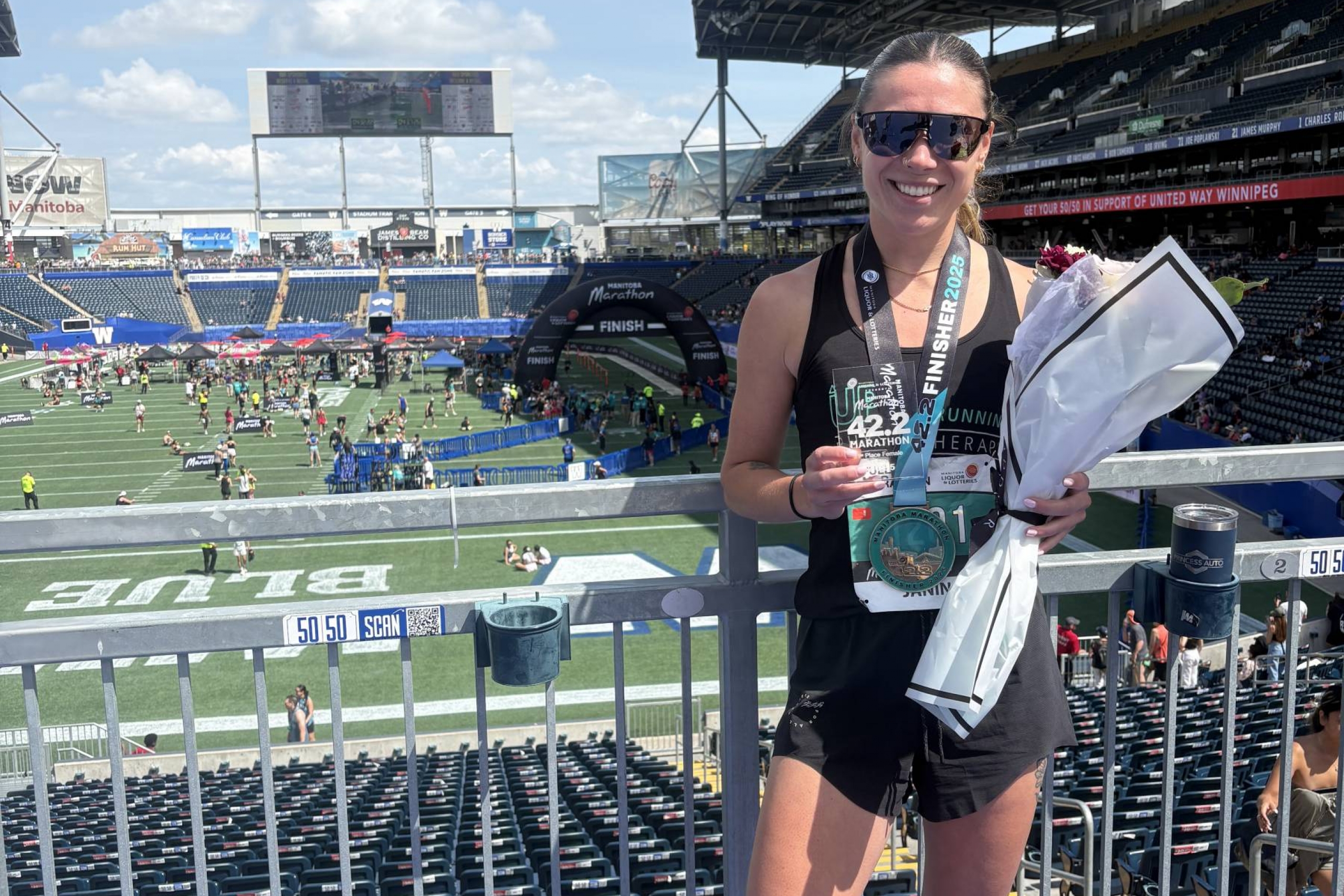 Woman wearing a medal, holding a trophy and flowers in a stadium.