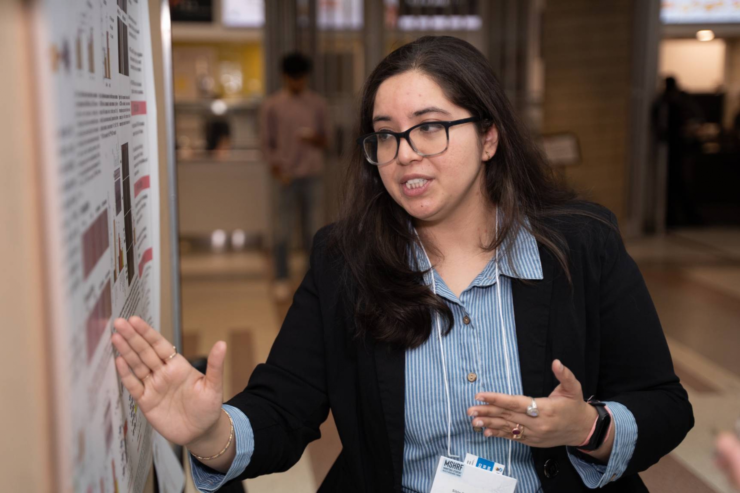 Sikta presents her research, gesturing towards her poster.