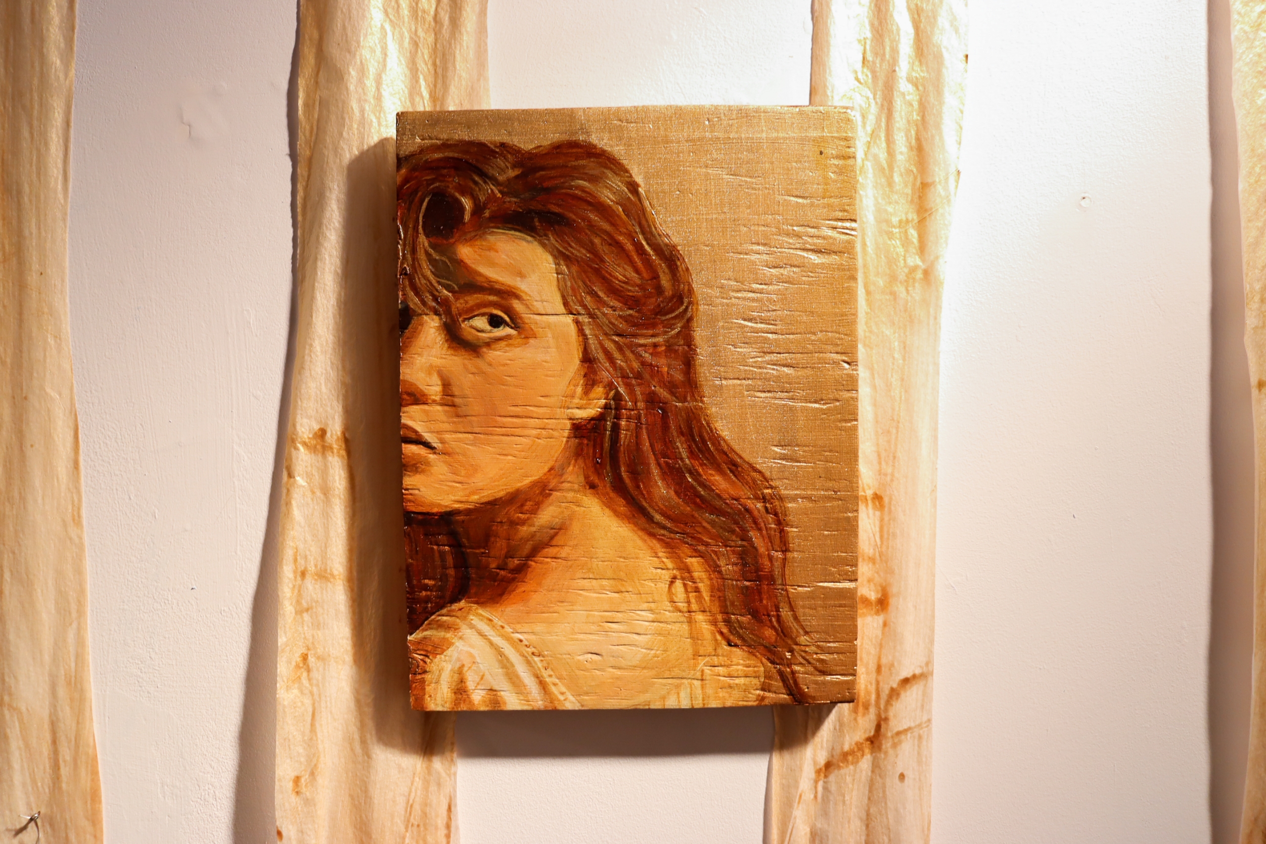 Close-up of a small wood panel painting showing a woman’s face in profile with long hair, mounted between two vertical fabric strips.