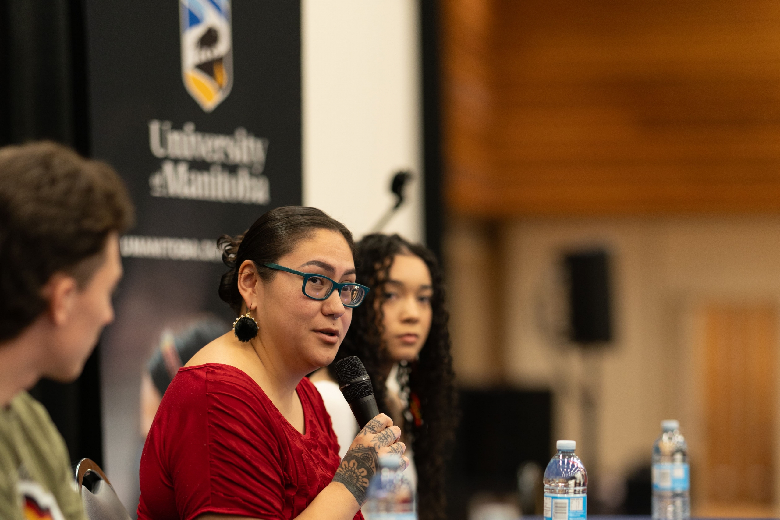 Students sat at table share a microphone, sharing with crowd.