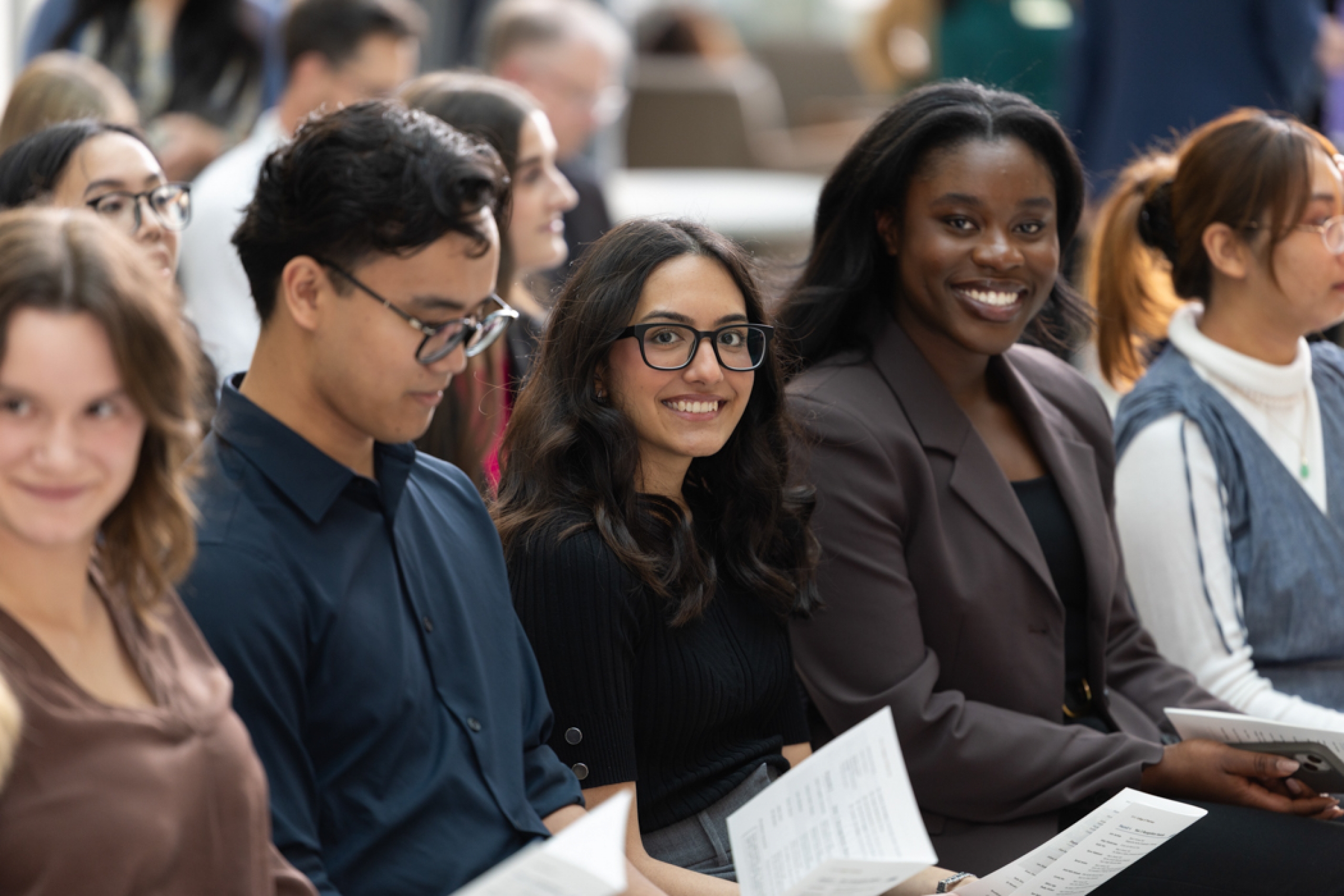 Students sit together; two of them smile at the camera.