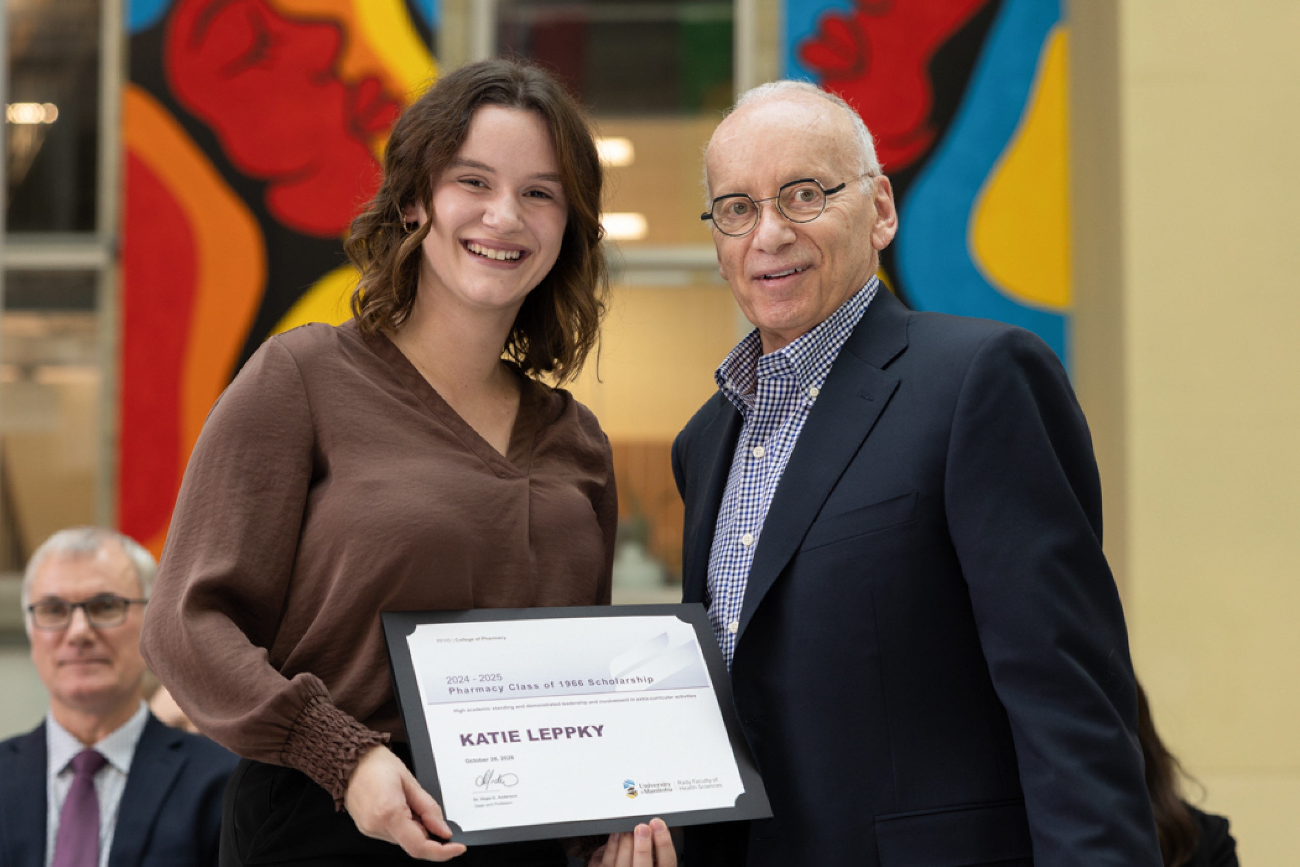 Katie Leppky and Lyle Silverman smile at the camera while Leppky holds an award certificate.