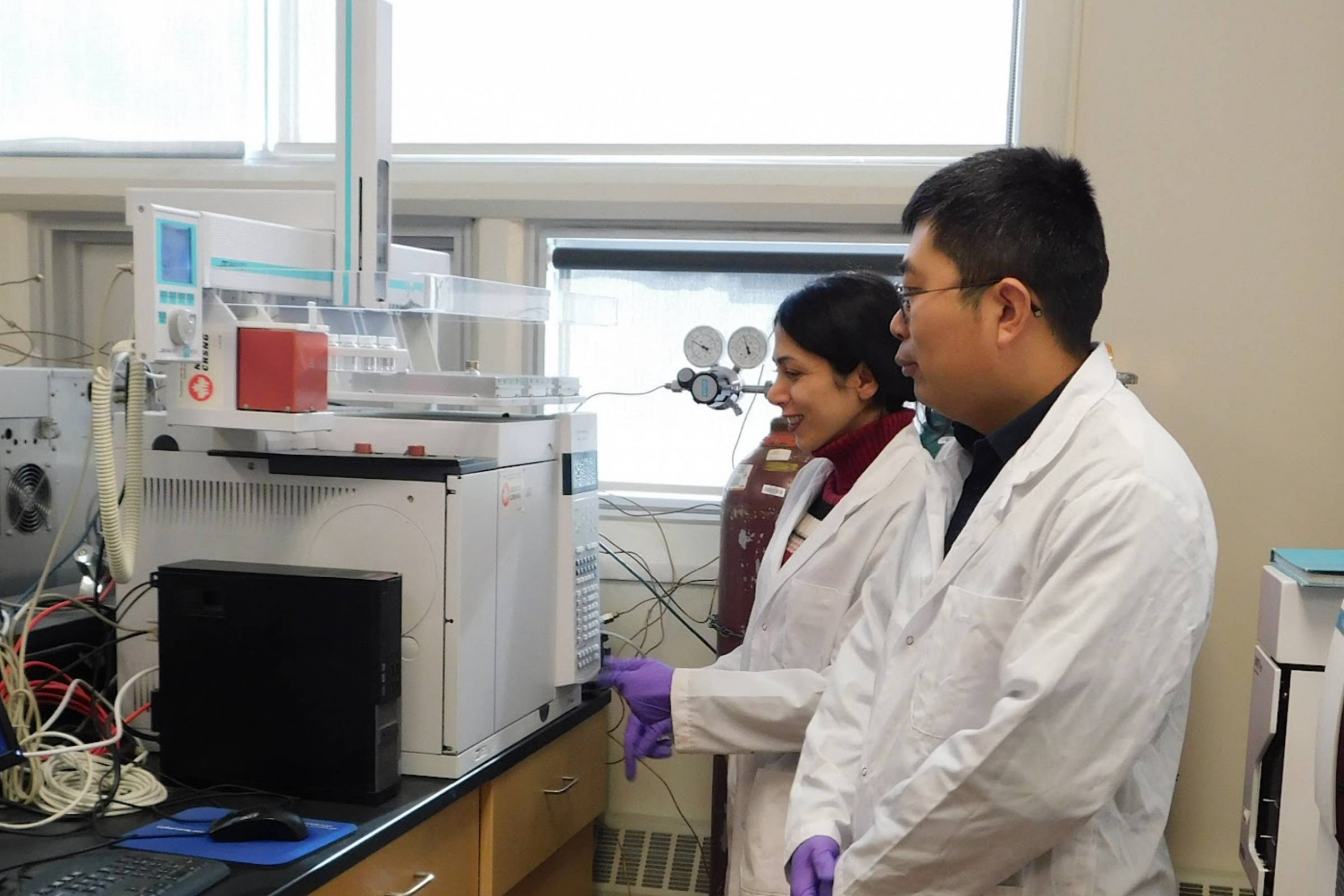 Two scientists in white coats stand in front of a machine in the lab