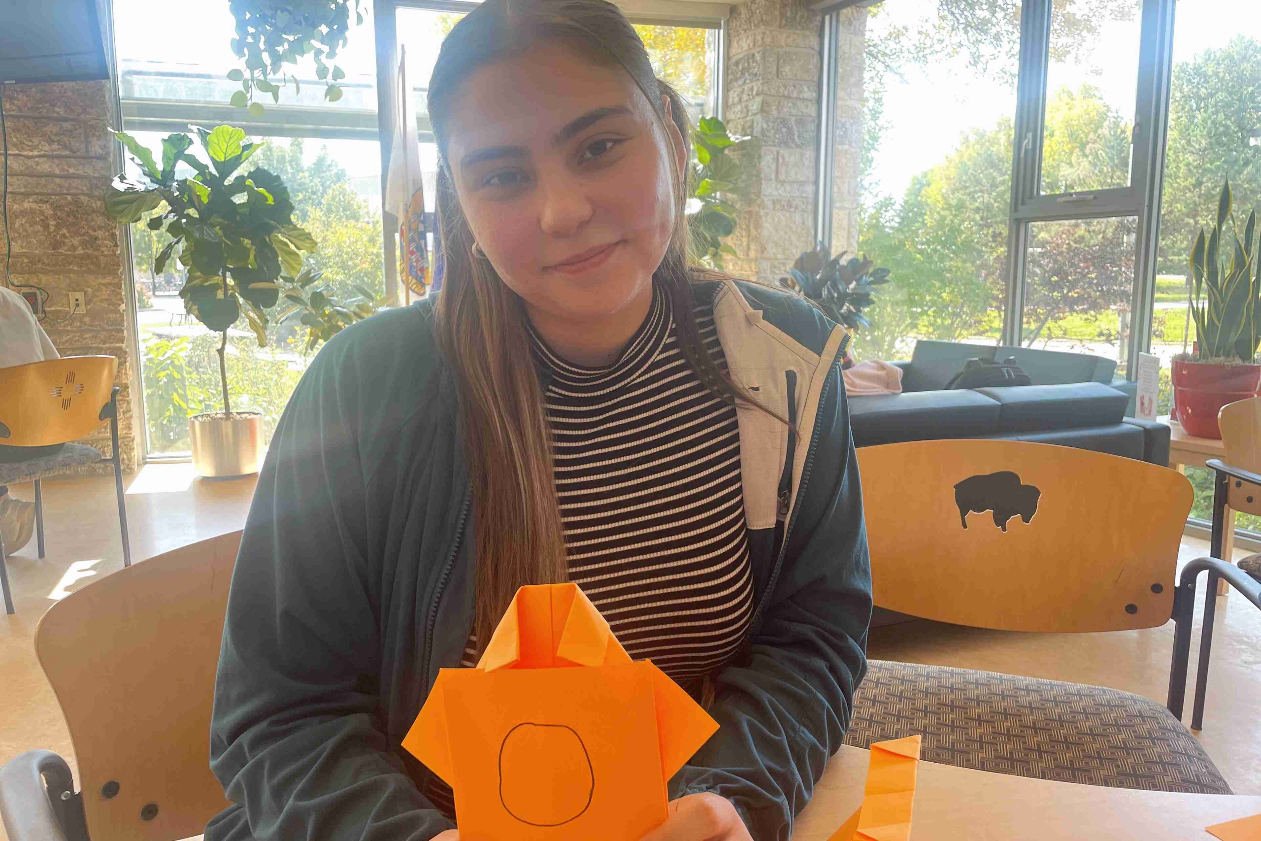 A student holds of her origami orange shirt.