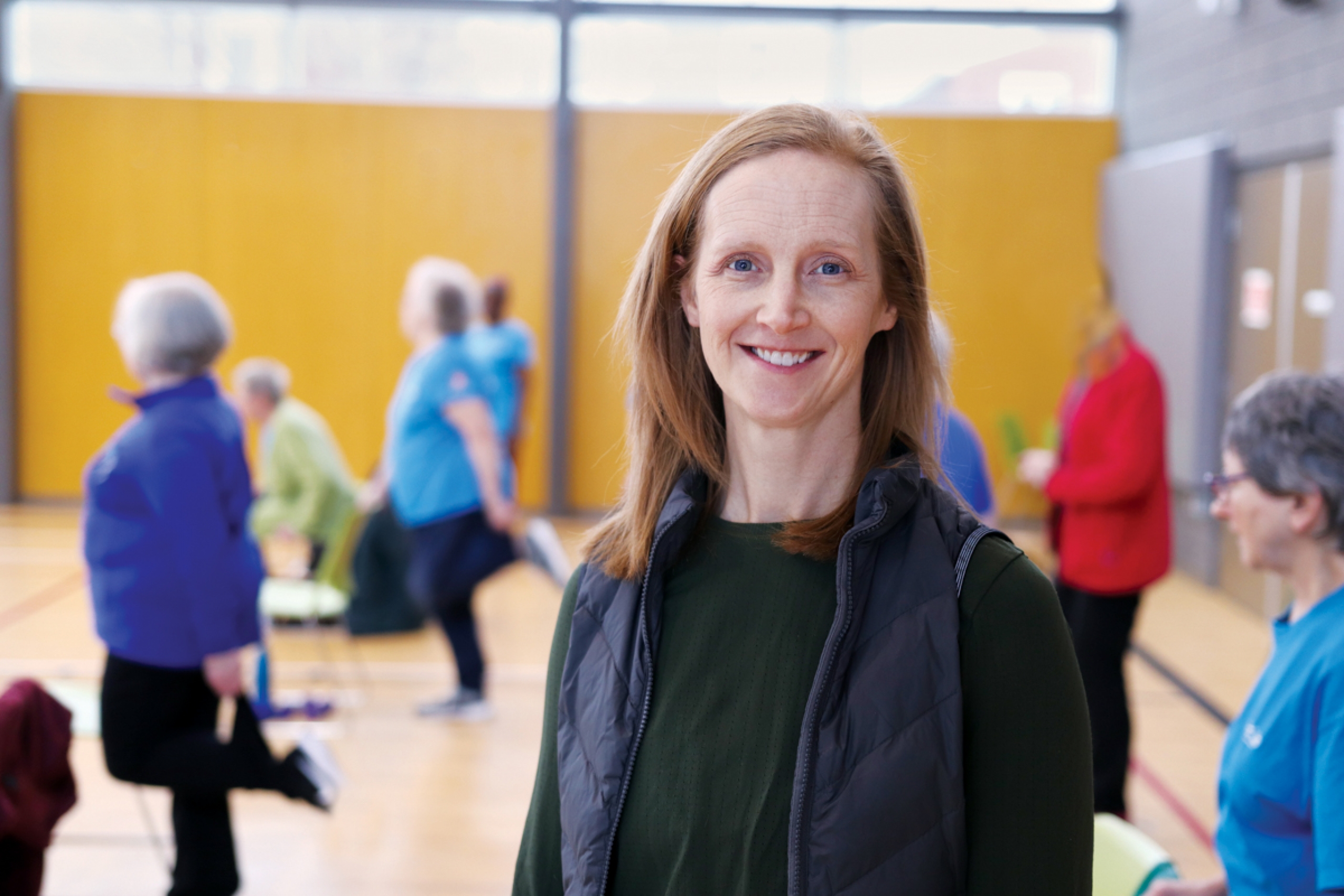 Kate Sibley smiles at the camera, in the background you can see a group of seniors working out.