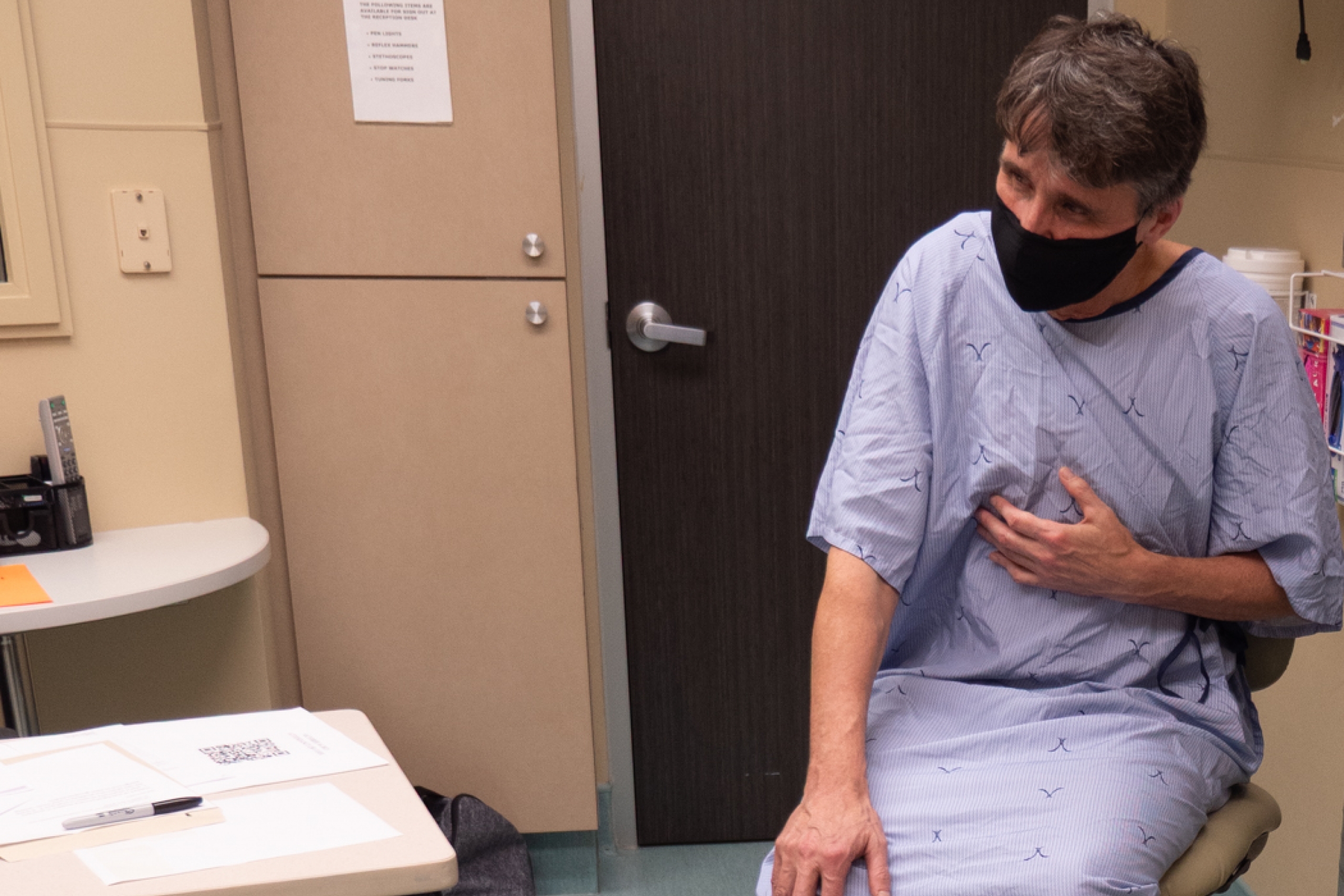 A Standardized Patient wearing a hospital gown and face mask, acting out a clinical scenario.