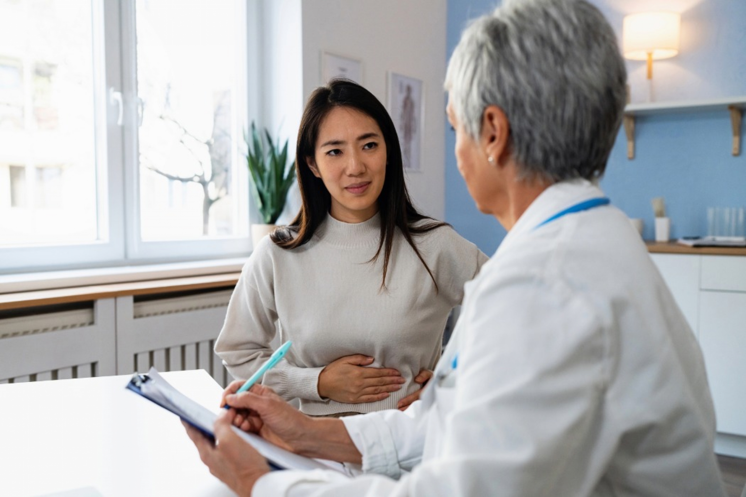 Patient describes stomach ache symptoms to doctor stock photo.