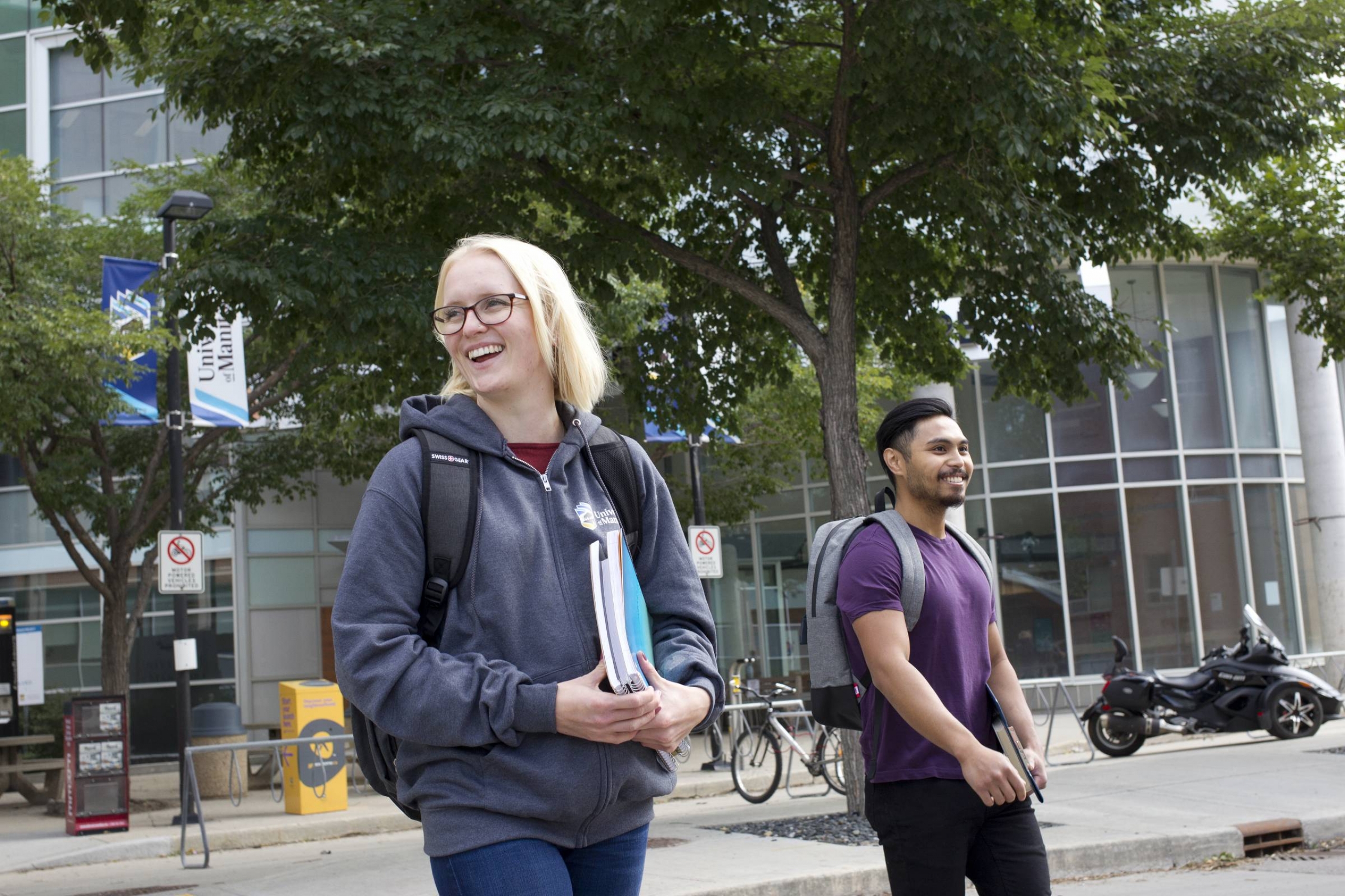 Two smiling students walk outside with notebooks.