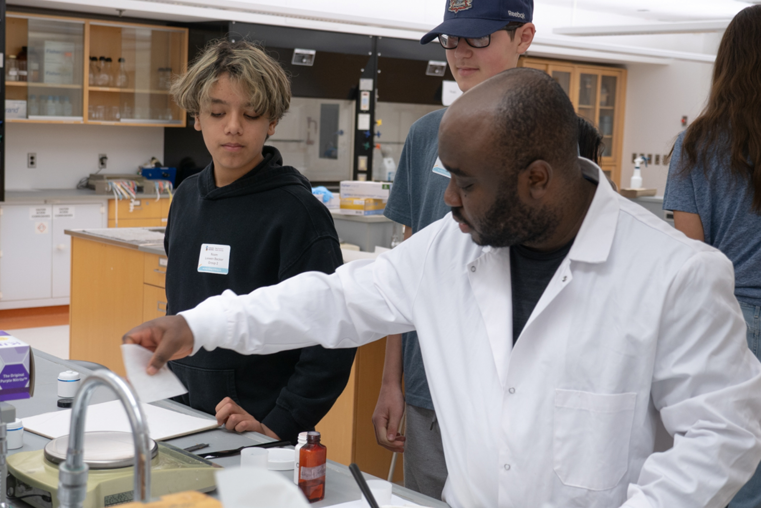 An instructor guides two students through a practical lab exercise.